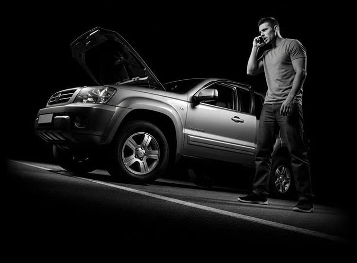 Driver on the phone beside an SUV with its hood up, on a dark road at night
